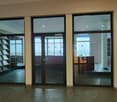 Large glass entrance doors, empty room, concrete floor, glass shelves on left, large window on right.
