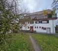 white house, brown roof, wooden fence, balcony, raised ground floor, garden