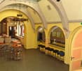 A large room with arched ceilings, yellow walls, and a wooden floor. There are tables and chairs, a chandelier, and a bar counter with stools. There are also lamps hanging from the ceiling.