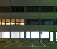 Modern commercial building, with several glass windows, green exterior, parking lot with several parking spots, sign for parking.
