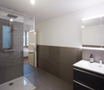 Modern glass enclosed shower, white sink with modern faucet, mirror with built-in lighting