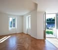 empty room, wooden floor, white walls, three windows, open door leading to balcony with garden view