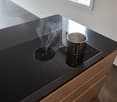 Modern induction cooktop with digital controls, steam rising from pot, sleek black countertop.