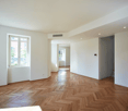 Empty room, wooden parquet flooring, white walls, large window, corridor leading to other rooms.