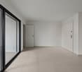 Spacious room with large sliding glass doors, white walls, and light-colored tile flooring. The room appears to be empty, with a white door visible on the right side.