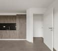 Open-concept kitchen and living area, gray concrete-style cabinets, black countertops, white walls, gray tile flooring, white door leading to another room