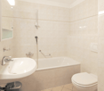 White bathroom with tiled walls and floors, a bathtub, a white sink with faucet, a white toilet, and a shower.