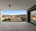 Large balcony or terrace with panoramic views of the surrounding buildings, mountains, and blue sky. The balcony has a tiled floor and is surrounded by glass walls, providing an open and unobstructed view of the scenic landscape.
