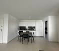 Open-concept kitchen and dining area with white cabinets, black countertops, and a dining table with chairs. Tile flooring throughout the space. Entrance door visible on the left side of the image.
