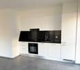 Modern white kitchen cabinets, black countertop, built-in oven, sink with faucet, tiled floor