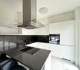 modern kitchen with black countertops, white cabinets, induction cooktop, oven, sink, faucet, and a glass range hood