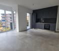 Open-concept living room and kitchen with large windows, modern black kitchen cabinets and appliances, and access to a balcony or terrace.