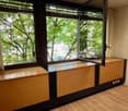 Large windows overlooking a lush, green outdoor area, wooden floors, built-in storage units or cabinets with a wooden finish.