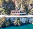 building on a cliffside, above a river, near cars and a bridge