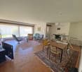 Spacious living room with hardwood floors, large windows, comfortable seating area with armchairs and a sofa, dining table, and various decor items.