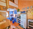 modern kitchen, blue cabinets, white refrigerator, wooden wall, sink, microwave, oven, plant, trash bin, basket, fireplace
