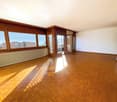 Empty room with wooden floor, white walls, large windows with balcony access, radiator, wooden panels