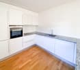 modern kitchen with white cabinets, granite countertops, stainless steel sink, oven, dishwasher, wooden floor