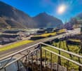Balcony with railings overlooking a road, a hillside with buildings, mountains in the background, sunny weather
