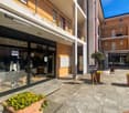 Commercial building, 3 stories, glass doors, metal railing, yellow flowers in planters, potted trees, sidewalk, balcony