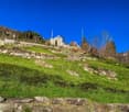 Large green grass with stone walls on side and background view of mountains and a house