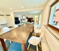 wooden table, 4 white chairs, carpet, fireplace visible in the background, flatscreen TV, couch, radiator, large window, chairs