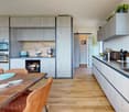 Modern kitchen with hardwood floor, wooden dining table, grey cabinets, modern appliances, sink, and faucet.