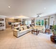 Modern living room with beige couches, beige tiled floor, open to a kitchen with a dining area, large windows, and potted plants