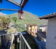 The image shows a residential area with colorful buildings, palm trees, and a mountainous backdrop. There is a red lantern-style light fixture visible on the balcony or terrace of one of the buildings.