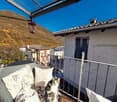 Cozy balcony with wicker furniture, pillows, and a cat enjoying the view of the surrounding buildings and mountains.