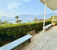 Outdoor area with a view of the mountains and lake, two white benches, and a hedge.