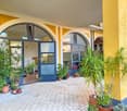 Yellow and white exterior, arched entrance, brick floor, multiple potted plants
