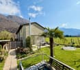 House with brick walls, green roof, garden with palm tree, patio with table and chairs, mountains in the background