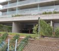 Modern apartment building with glass balconies, concrete structure, outdoor dining area, garden, and fenced yard
