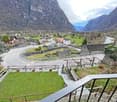 Mountain village with stone houses, winding road, river, and green fields