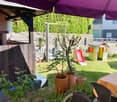 Covered patio area, potted plants, children's playhouse, grassy lawn, stone wall