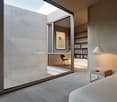 Spacious bedroom with large windows, concrete walls, hardwood floors, built-in shelving, and a small seating area with a chair.
