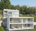 Modern two-story house with large glass windows, balconies, and surrounded by lush greenery