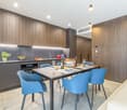modern kitchen with wooden cabinets, tile flooring, dining table with blue chairs, open to living area