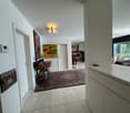 white walls, white tile floor, rug, wooden table, paintings, white door, white cabinet, glass door, living room