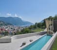 infinity swimming pool, tiled deck, modern landscaping, grass lawn, views of the city and mountains