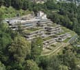 Modern building complex with green roofs, nestled in a hillside with lush greenery, panoramic views