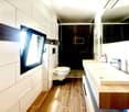 modern bathroom with white tiles, wooden floor, double sink, toilet, shower, window