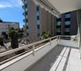 large balcony with tiled floor, metal railing, awning, view of the street and buildings