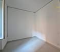 Empty room with white walls, gray floor, window, power outlets, and a radiator.
