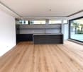 Large open-plan living space with hardwood flooring, black kitchen island, and large windows providing natural light