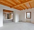 open layout, unfinished interior, wooden beams, power outlet on wall, window on the right, open doorway in the middle, wooden staircase to the right of doorway
