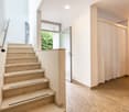 The image shows the interior of a residential property. It features a staircase with marble steps leading up to the second floor. The hallway has white walls and a curtain-covered doorway leading to another room. The floor is covered in a light-colored ca