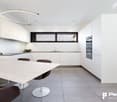 Modern, open-concept kitchen with white cabinets, black countertops, large window, built-in appliances including a dishwasher, and a dining table with chairs.