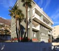 4 story building, gray exterior, red stripe, white windows, balconies, trees, hillside in background